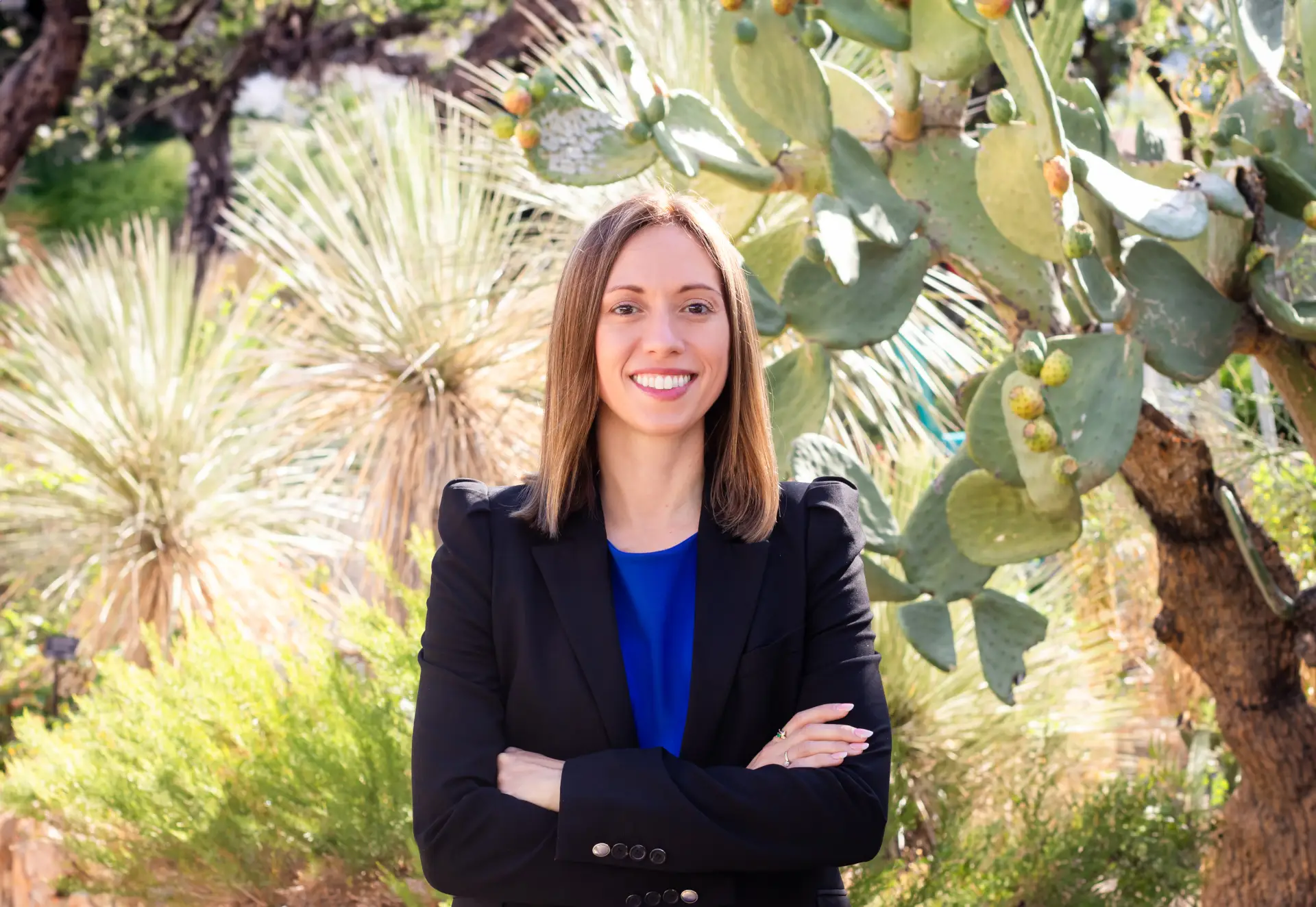 Image of Attorney White with black blazer and blue dress standing in front of cactus